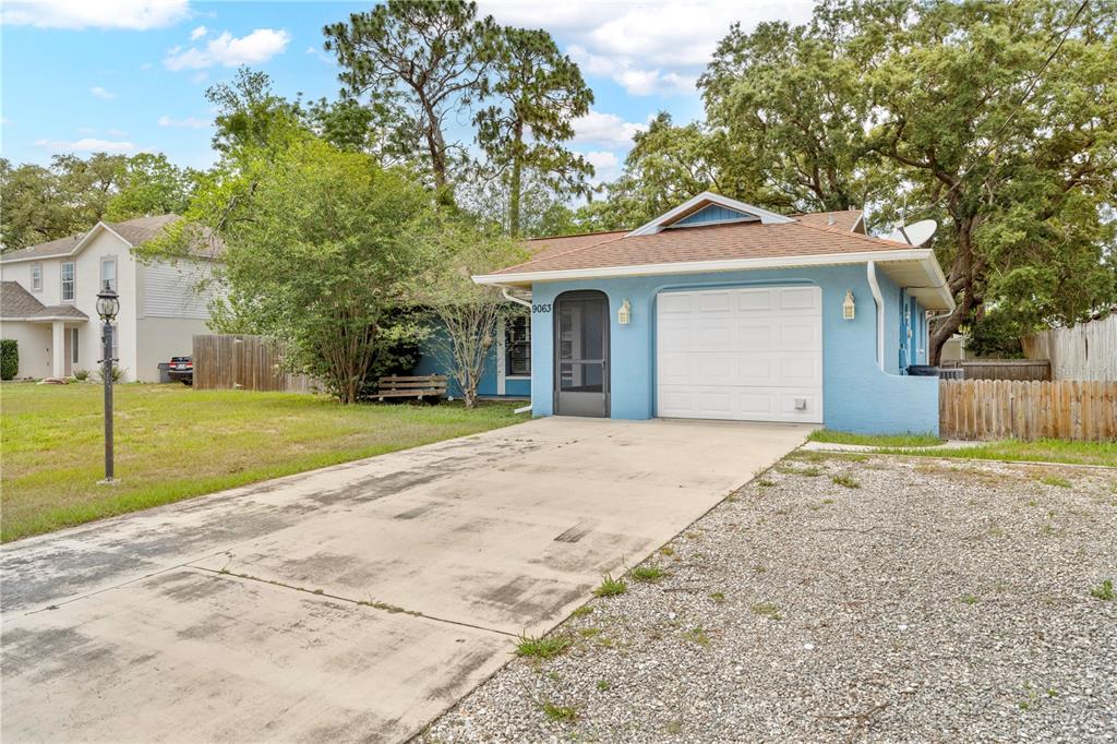 A light blue single-story house features a white garage door and a concrete driveway — 9063 PEMBERTON STREET, SPRING HILL, FL