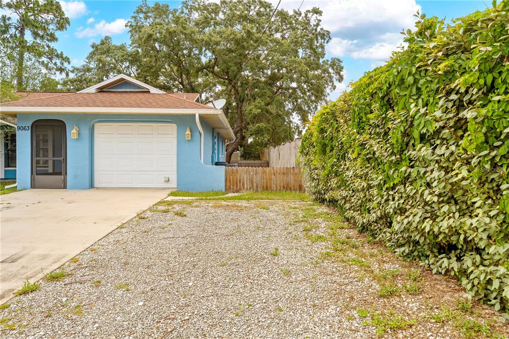 A light blue house with a gravel driveway and a large hedge on the right — 9063 PEMBERTON STREET, SPRING HILL, FL