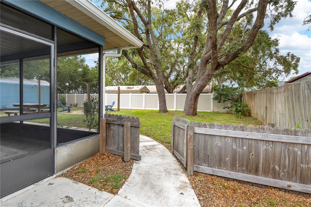 A concrete walkway leads from a screened-in porch through a wooden gate into a backyard — 9063 PEMBERTON STREET, SPRING HILL, FL