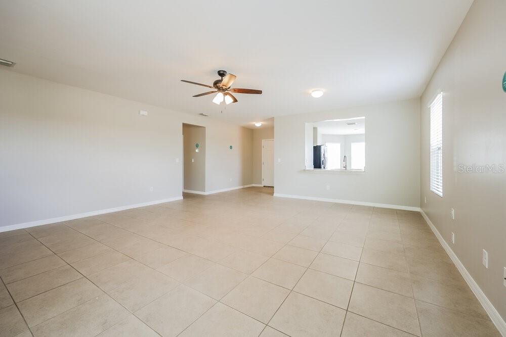 An empty living room with light tile flooring, a ceiling fan, and a kitchen pass-through — 627 SW 27TH TERRACE, CAPE CORAL, FL
