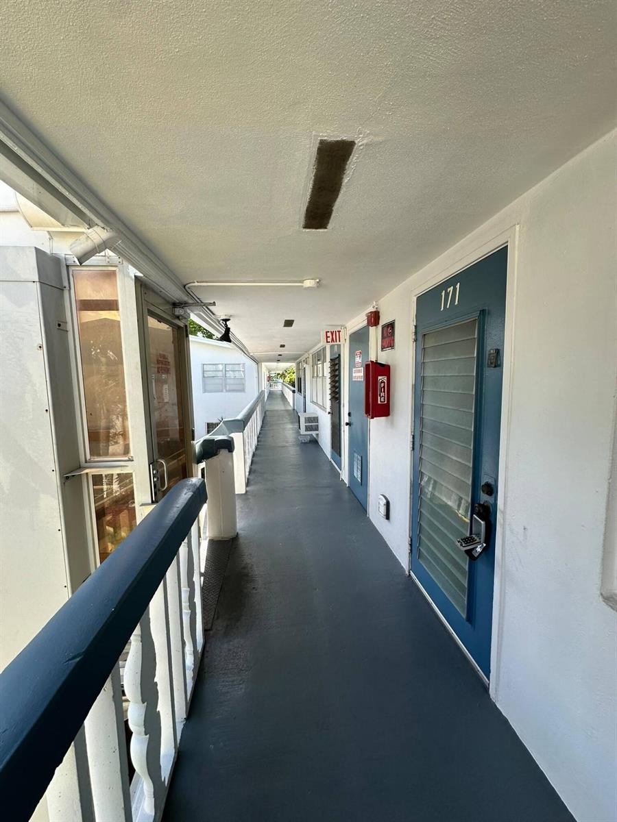 An outdoor apartment building walkway with blue doors, a fire extinguisher, and a metal railing — 171 Markham H # 171, Deerfield Beach FL 33442, DEERFIELD BEACH, FL