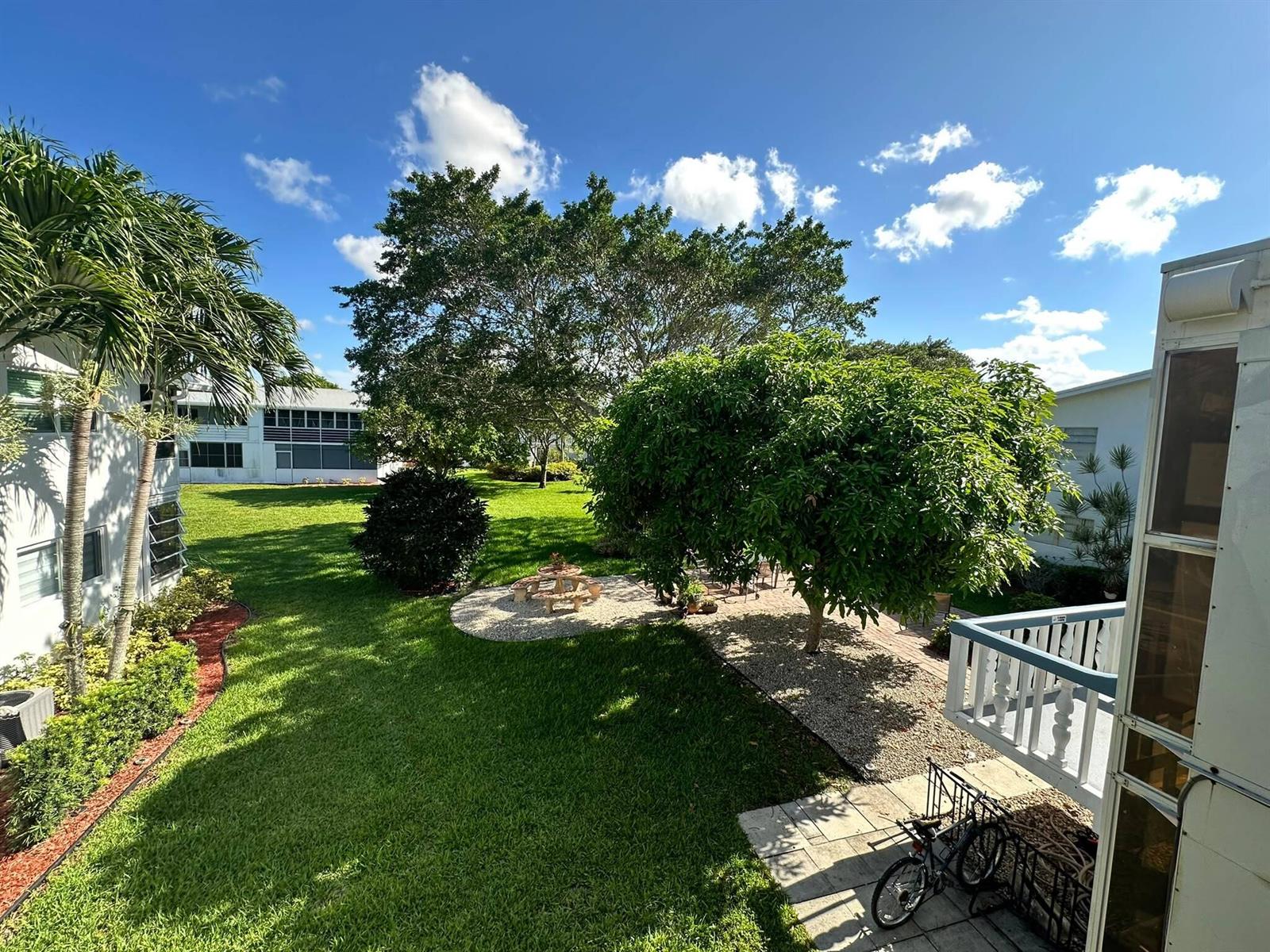 A view from a balcony overlooking a grassy backyard with trees and a patio area — 171 Markham H # 171, Deerfield Beach FL 33442, DEERFIELD BEACH, FL