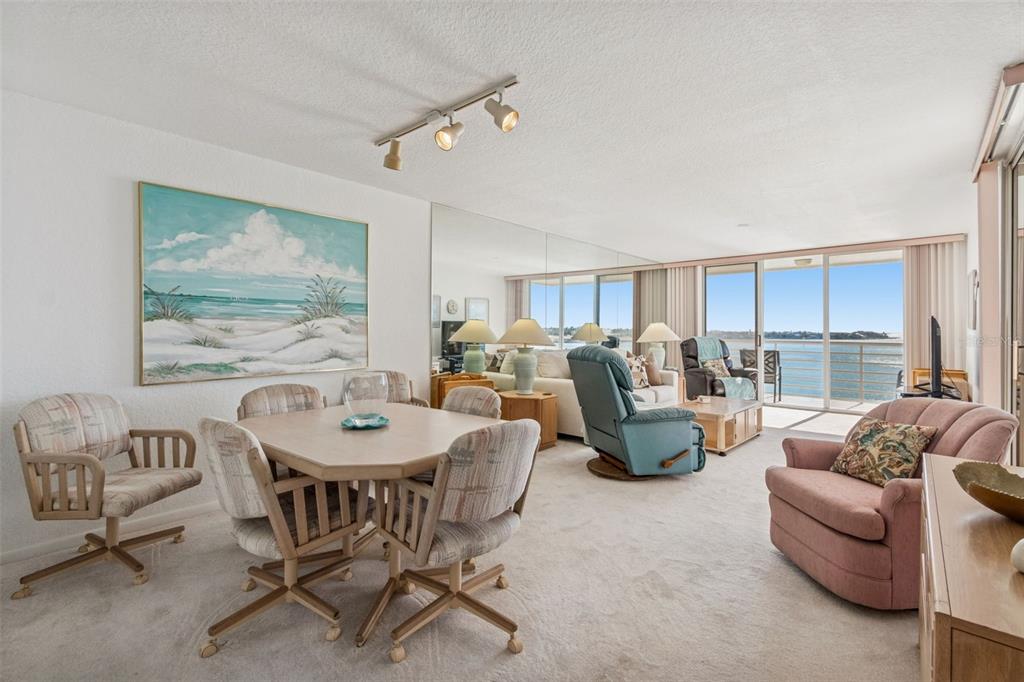 A dining area and living room with carpeted floors, mirrored walls, and a waterfront balcony view — 6105 BAHIA DEL MAR CIRCLE UNIT 686, ST PETERSBURG, FL