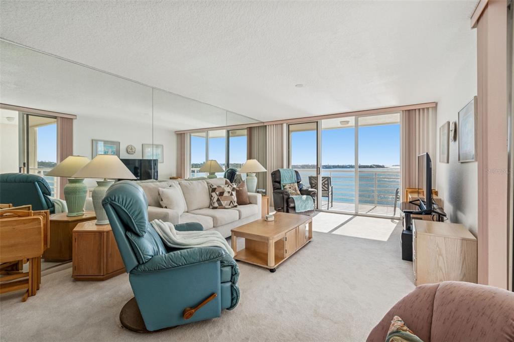 A living room features a blue recliner, a beige sofa, mirrored walls, and a balcony view — 6105 BAHIA DEL MAR CIRCLE UNIT 686, ST PETERSBURG, FL