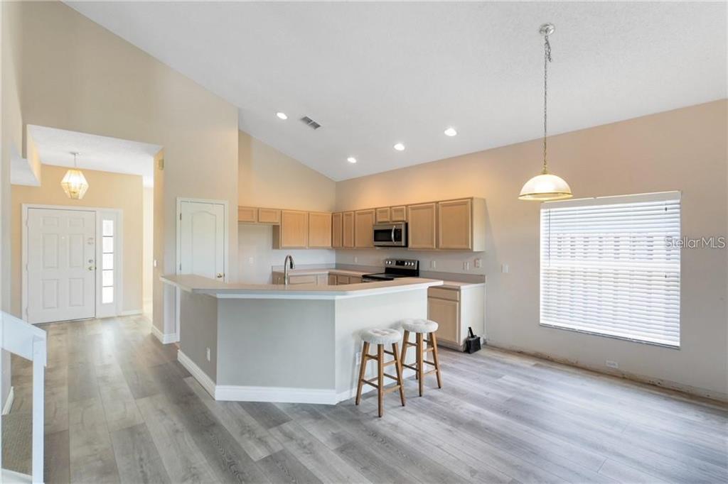 An open-concept kitchen features light wood cabinets, a breakfast bar with stools, and wood-look flooring — 3701 SEMINOLE DRIVE, ORLANDO, FL