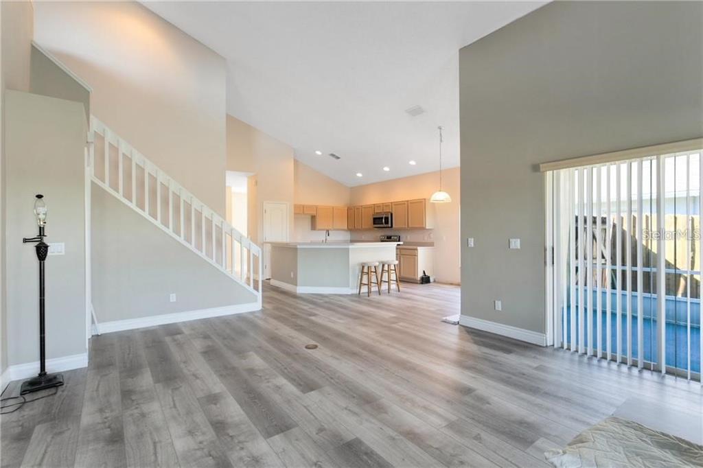 An open-concept living area features light wood-look flooring, a staircase, and a kitchen with bar seating — 3701 SEMINOLE DRIVE, ORLANDO, FL