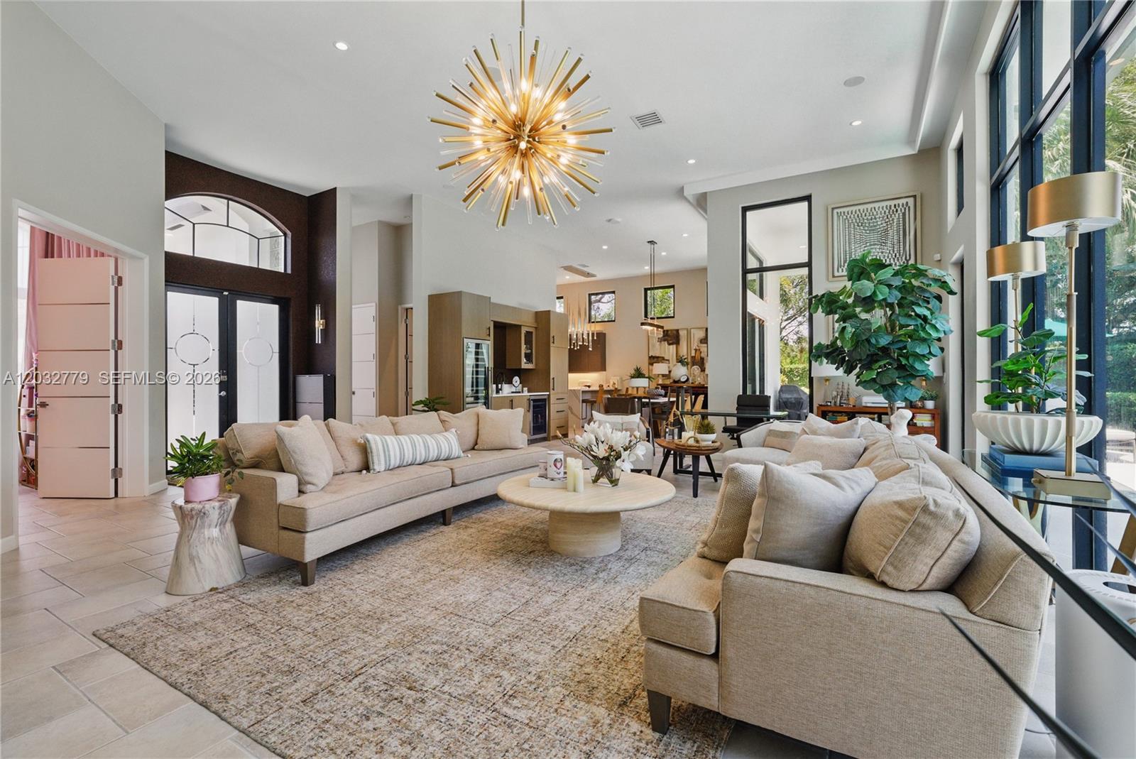 A spacious living room features a large starburst chandelier, neutral sofas, and floor-to-ceiling windows — 1755 SW 4th Ave, Boca Raton FL 33432, BOCA RATON, FL