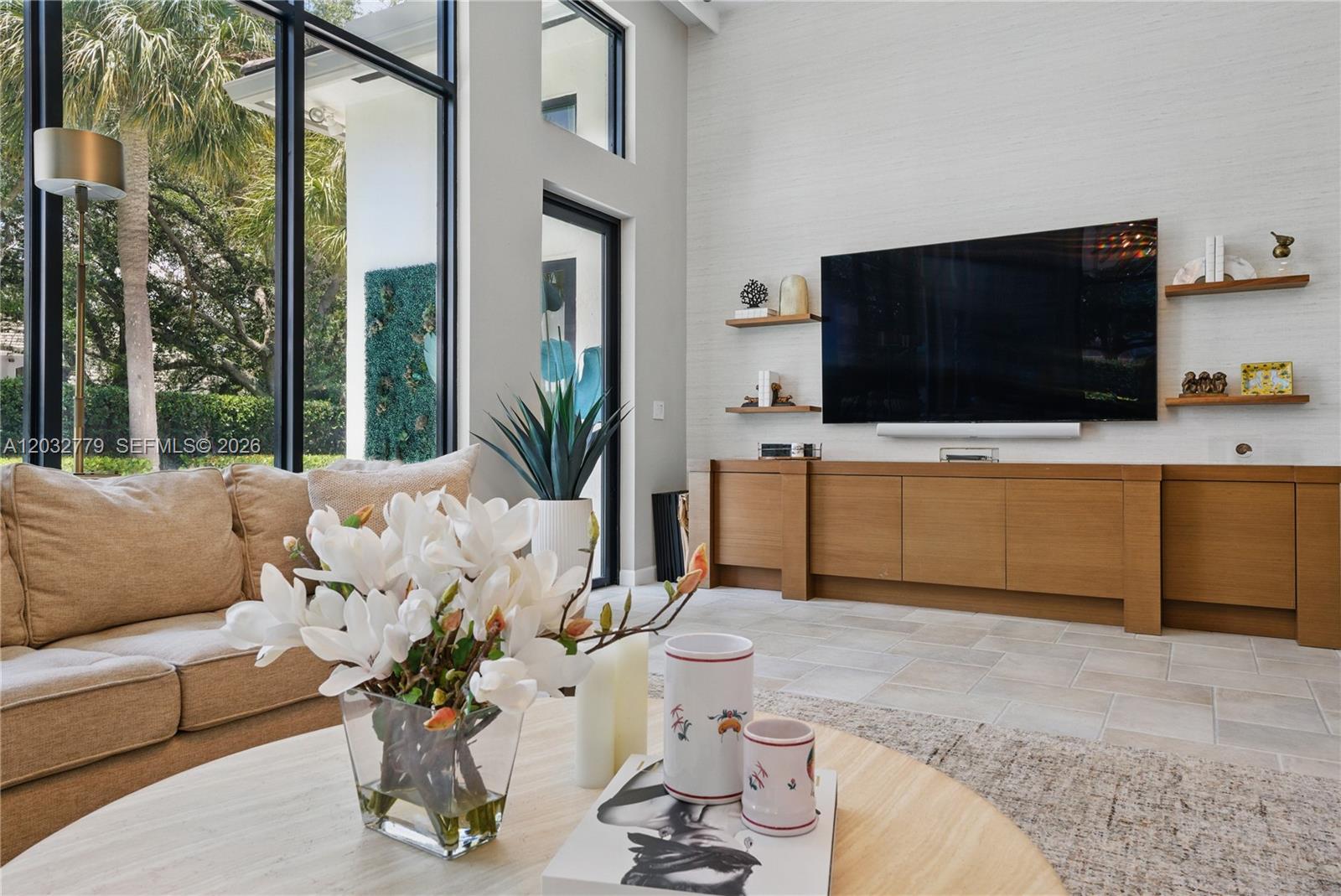 A living room features a large television, wooden cabinetry, floating shelves, and floor-to-ceiling windows — 1755 SW 4th Ave, Boca Raton FL 33432, BOCA RATON, FL