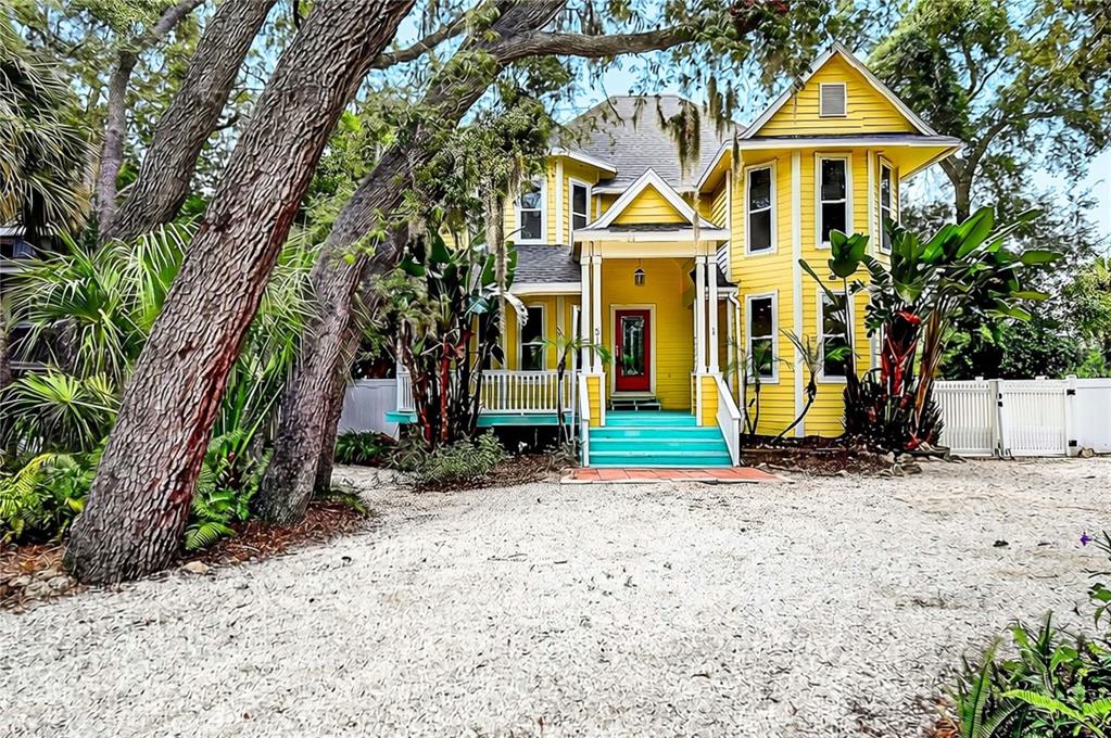 A yellow two-story house with a red front door and teal stairs sits behind trees — 510 WIDEVIEW AVENUE, TARPON SPRINGS, FL