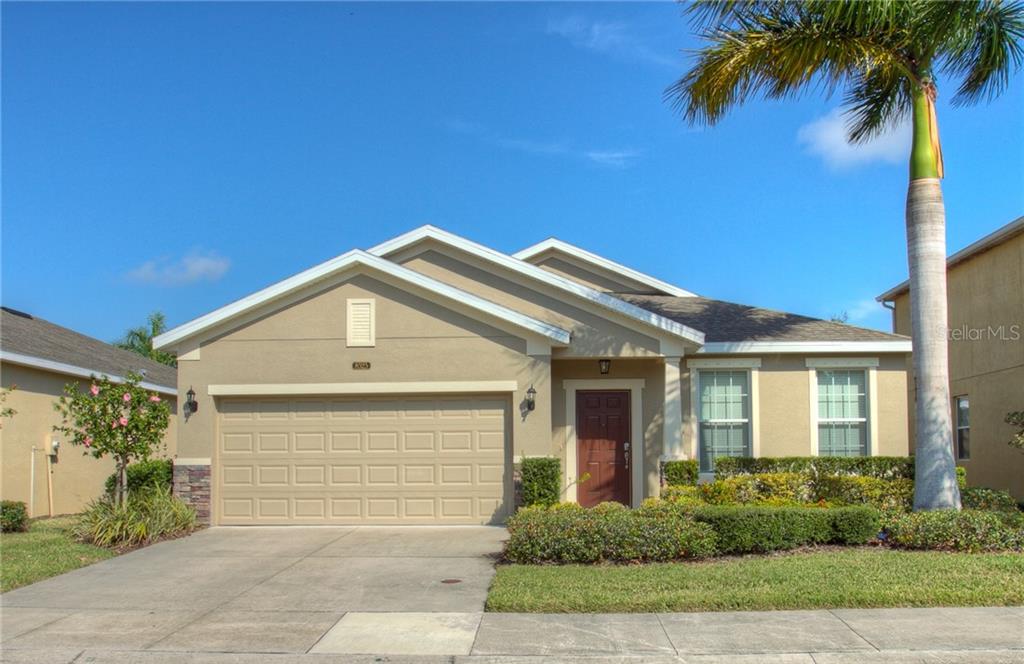 A single-story suburban house with a tan stucco exterior, a two-car garage, and a palm tree — 8525 KARPEAL DRIVE, SARASOTA, FL