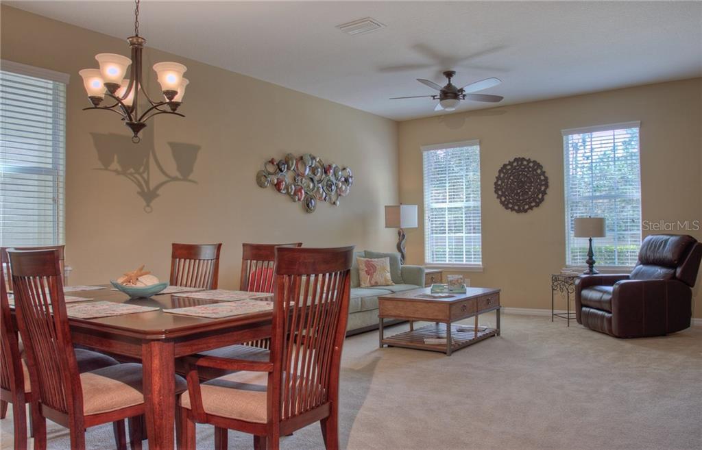 A dining area with a wooden table and chairs sits adjacent to a carpeted living room — 8525 KARPEAL DRIVE, SARASOTA, FL