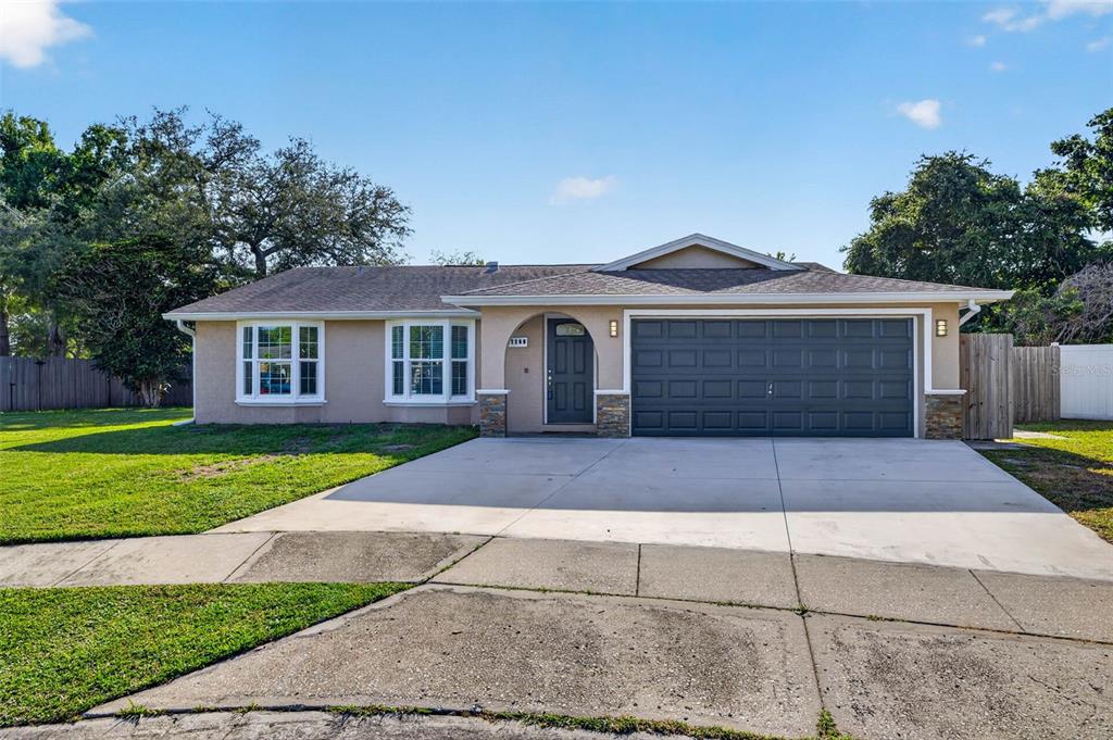 A single-story house with a tan exterior, a gray garage door, and a concrete driveway — 11280 FREEDOM COURT, SEMINOLE, FL