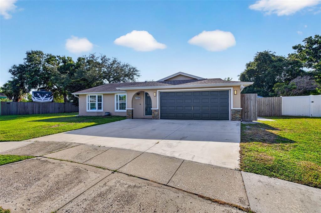 A single-story house with a tan exterior, dark garage door, and a concrete driveway — 11280 FREEDOM COURT, SEMINOLE, FL