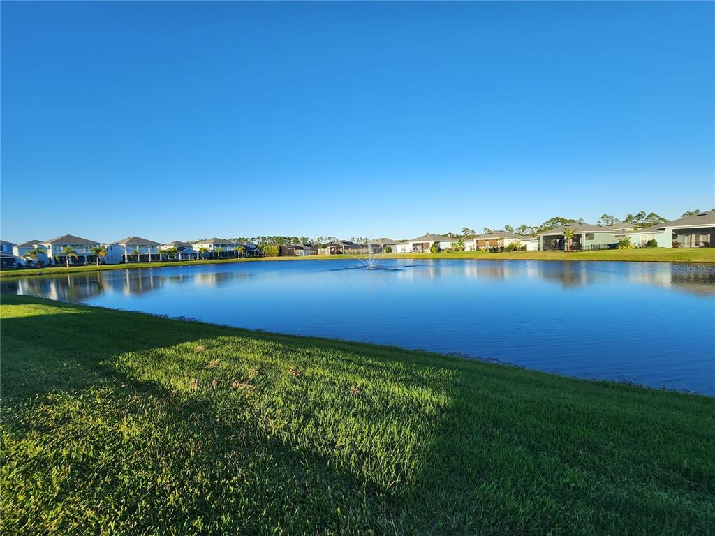 A view of a residential pond with a fountain surrounded by houses under a clear sky — 2937 MELETO BOULEVARD, NEW SMYRNA BEACH, FL