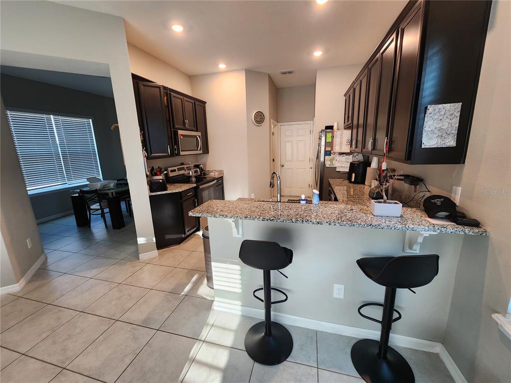 A kitchen features dark wood cabinets, granite countertops, a breakfast bar with stools, and tile flooring — 2937 MELETO BOULEVARD, NEW SMYRNA BEACH, FL