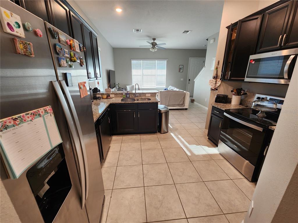 A kitchen with dark cabinets, stainless steel appliances, and tile flooring opens to a living area — 2937 MELETO BOULEVARD, NEW SMYRNA BEACH, FL