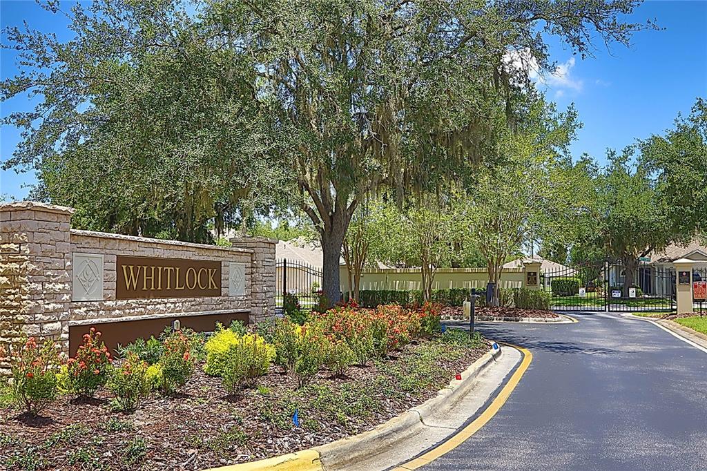 A stone entrance sign for a community named Whitlock sits beside a gated road — 31007 PROUT COURT, WESLEY CHAPEL, FL