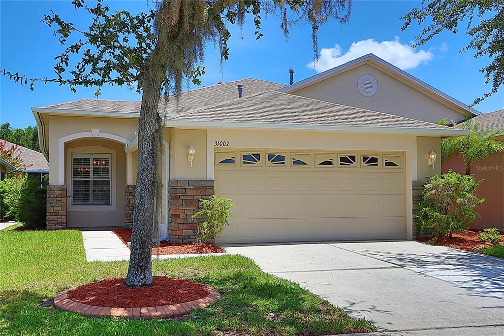 A single-story house with a beige stucco exterior, stone accents, and a two-car garage — 31007 PROUT COURT, WESLEY CHAPEL, FL