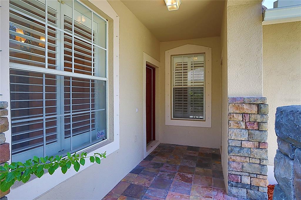 A covered entryway features tiled flooring, stone accents, and a front door with a window — 31007 PROUT COURT, WESLEY CHAPEL, FL
