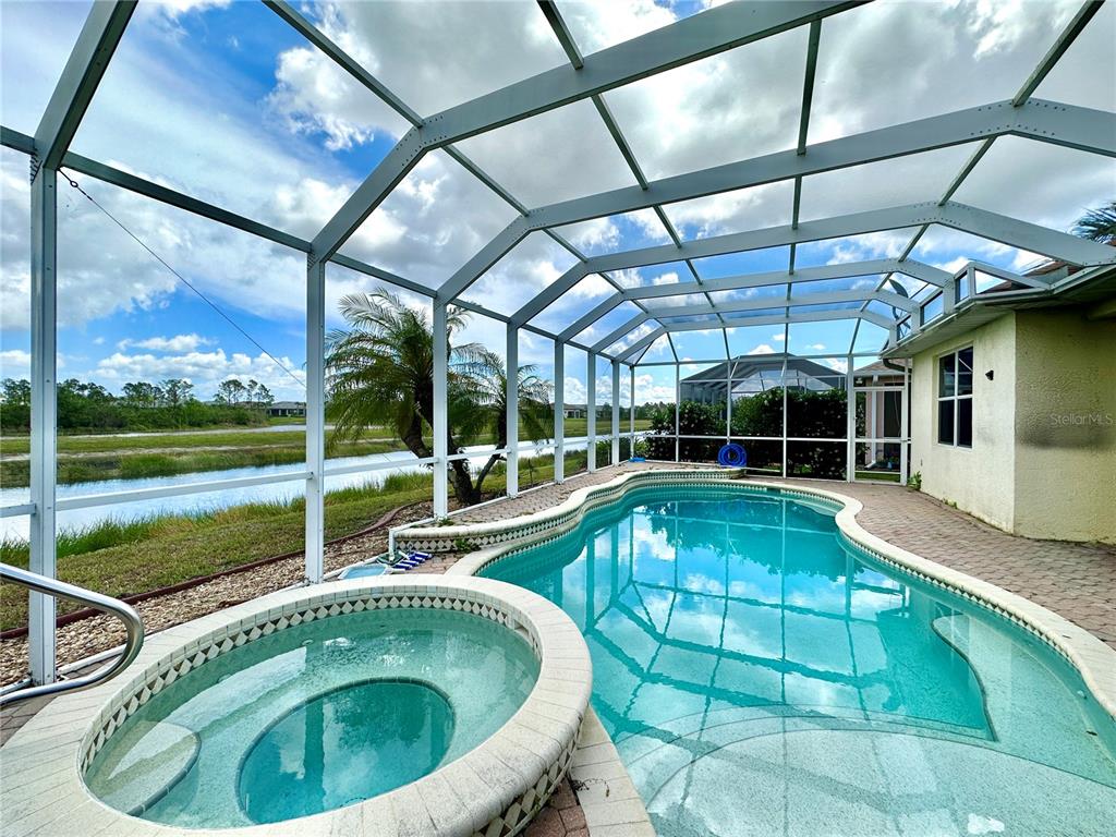 A screened-in pool and spa area overlooks a canal with a grassy bank — 1799 SCARLETT AVENUE, NORTH PORT, FL