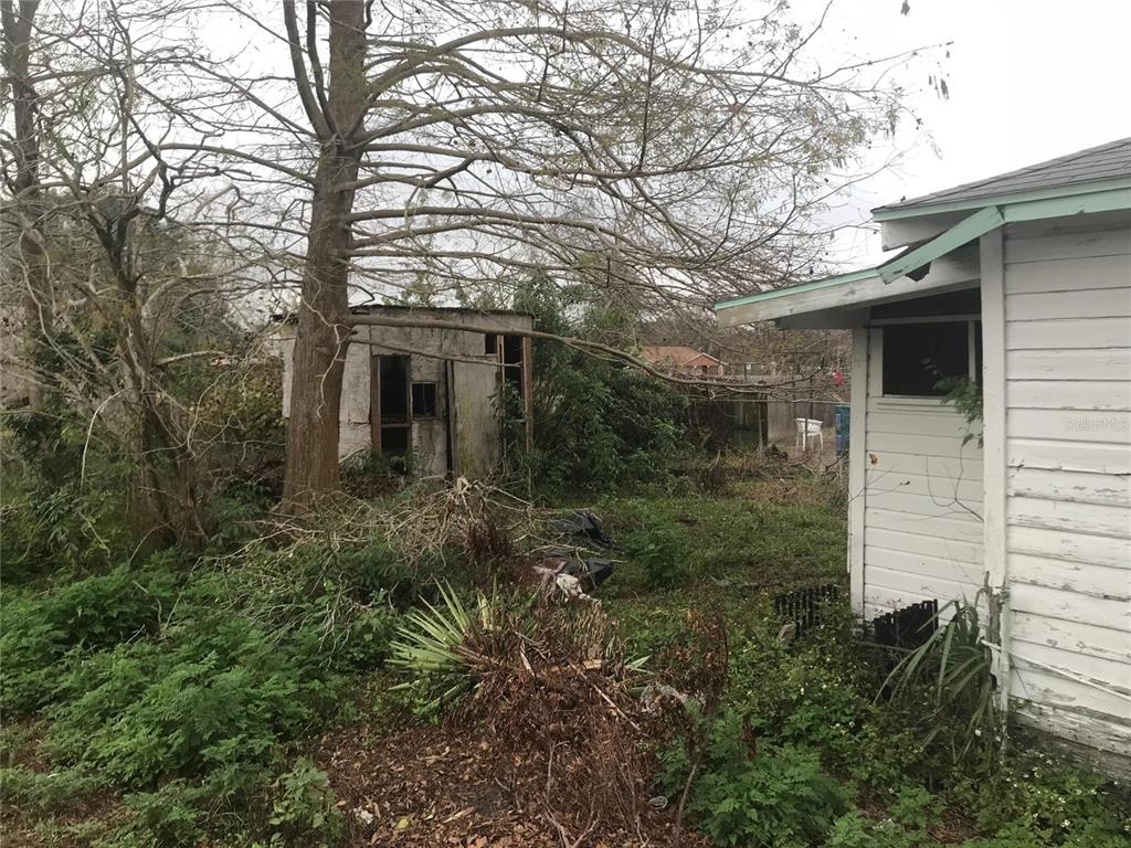 A weathered shed stands in a brush-filled backyard next to a white wooden house — 2340 BROADWAY STREET, SANFORD, FL