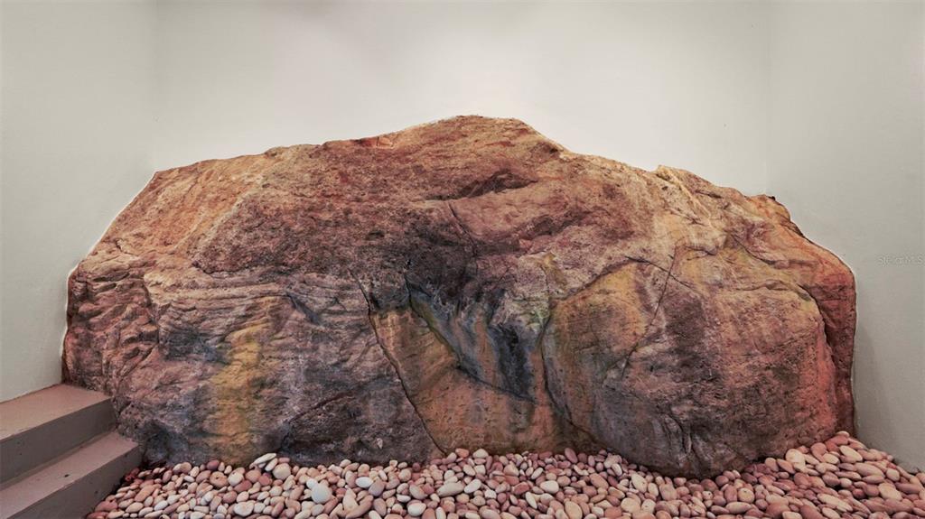 A large decorative rock formation sits against a white wall above a bed of stones — km 16.5 PR-15, CAYEY, PR