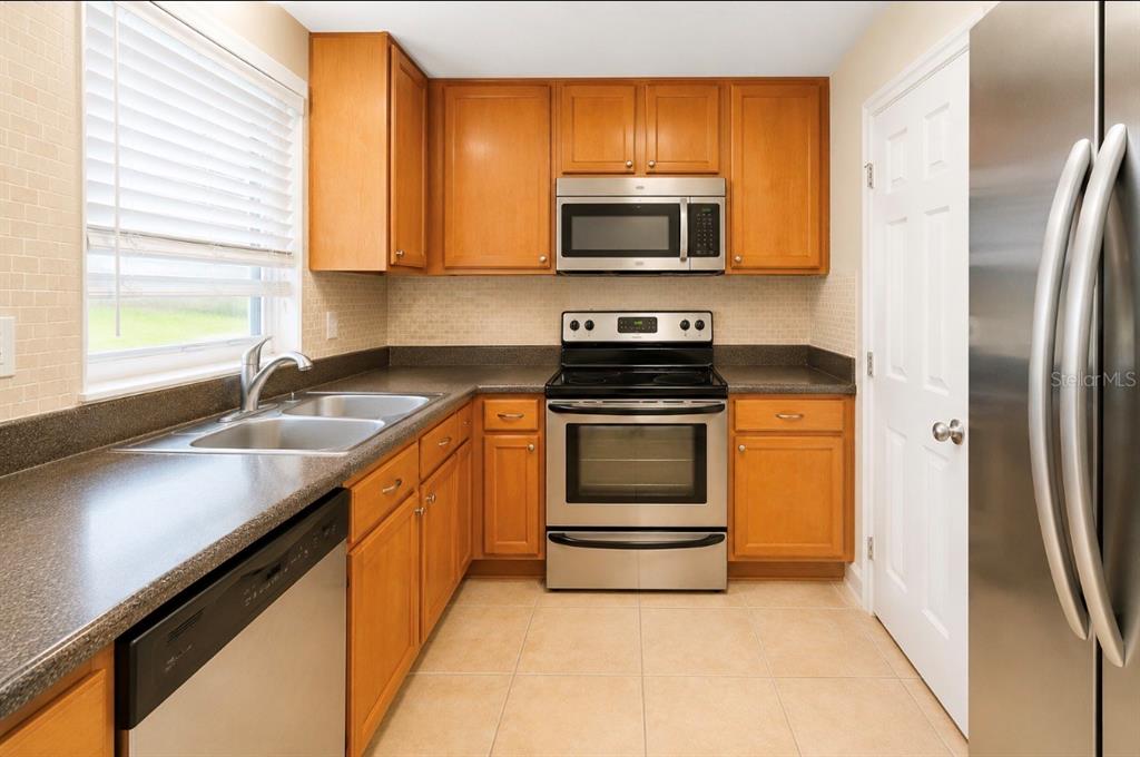 A kitchen with wood cabinets, stainless steel appliances, a double sink, and tile flooring — 4312 HECTOR COURT UNIT 4, ORLANDO, FL
