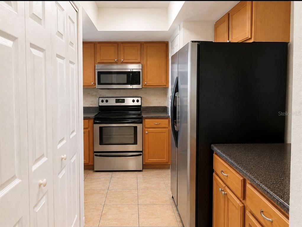 A kitchen features wood cabinets, stainless steel appliances, a black refrigerator, and tile flooring — 4312 HECTOR COURT UNIT 4, ORLANDO, FL