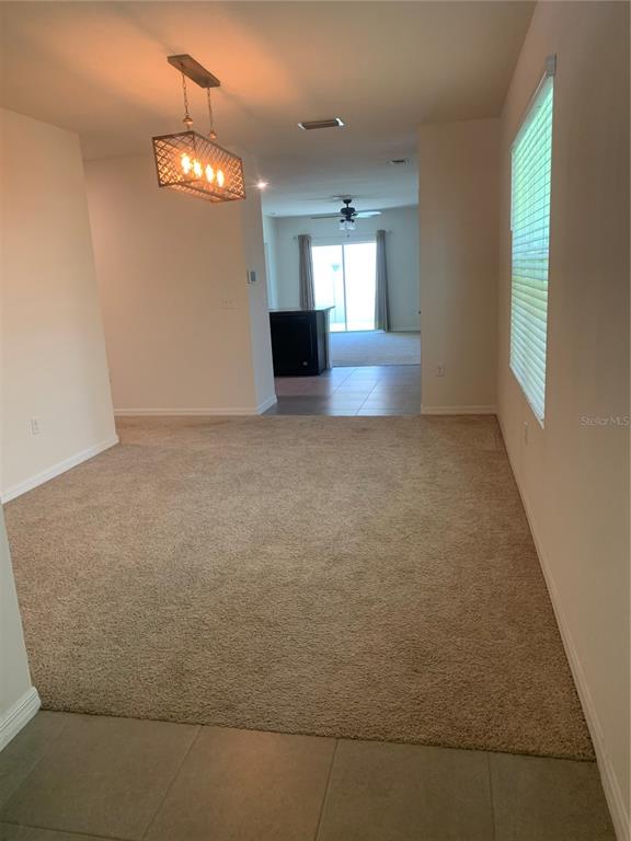 A carpeted dining area features a rectangular pendant light fixture and leads to a kitchen — 10977 CARLTON FIELDS DRIVE, RIVERVIEW, FL