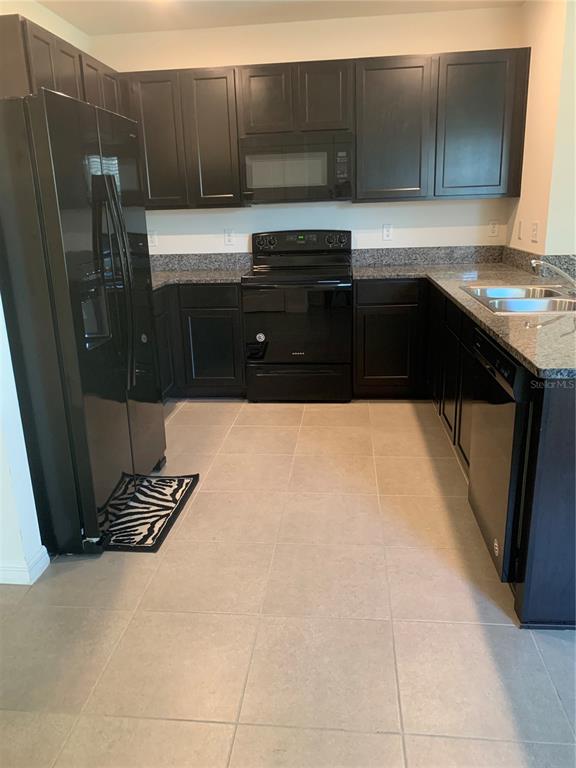 A kitchen features dark wood cabinets, black appliances, granite countertops, and light-colored tile flooring — 10977 CARLTON FIELDS DRIVE, RIVERVIEW, FL