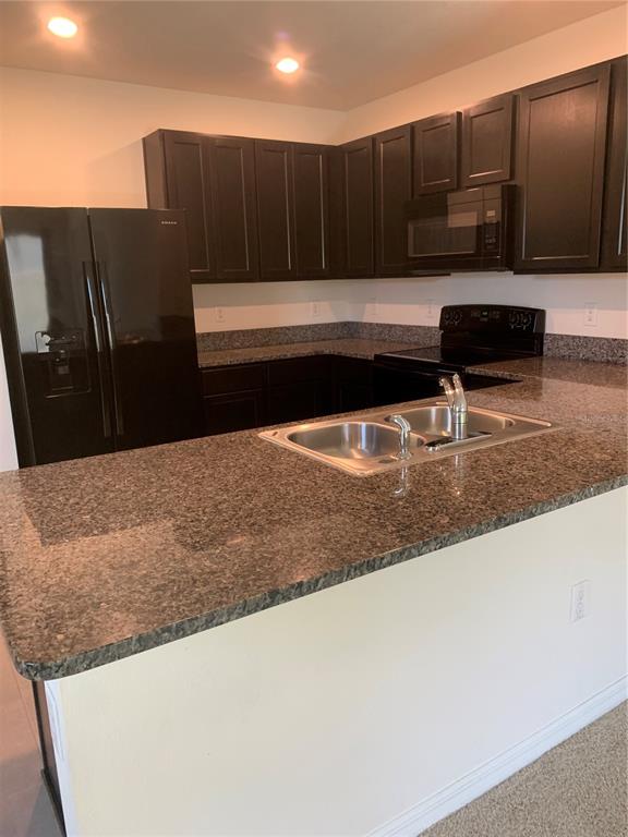 A kitchen features dark wood cabinets, granite countertops, and black appliances — 10977 CARLTON FIELDS DRIVE, RIVERVIEW, FL