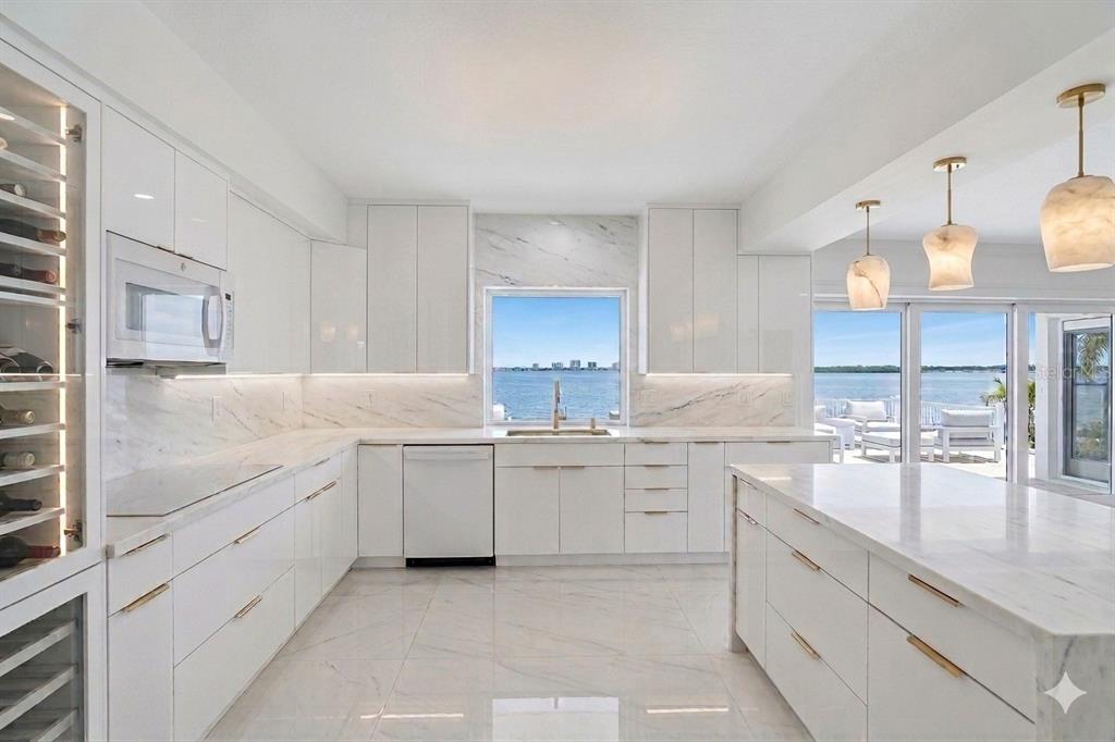A modern white kitchen features marble countertops, a wine rack, and a view of the water — 891 ISLAND WAY, CLEARWATER BEACH, FL