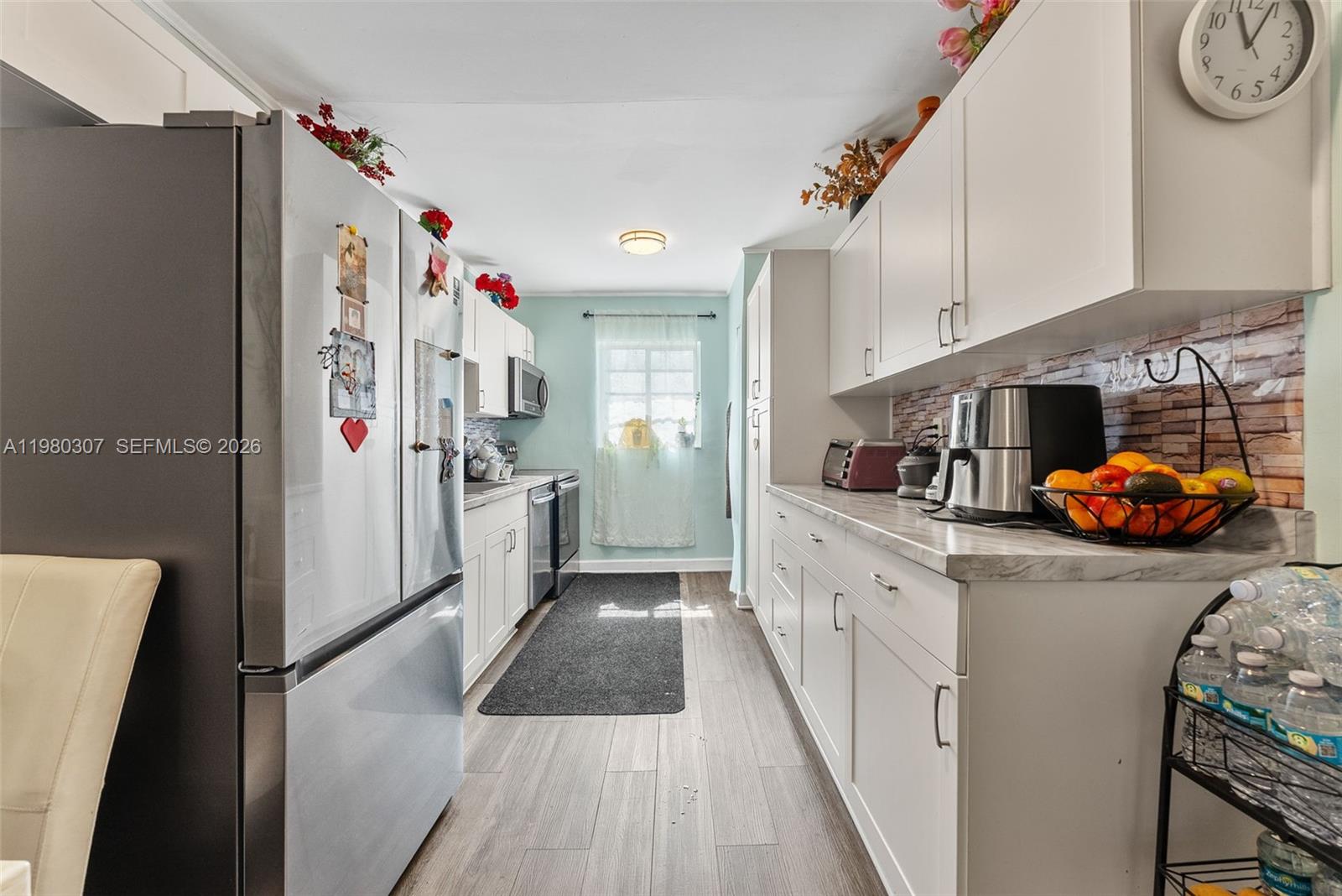 A galley kitchen features white cabinets, stainless steel appliances, and a faux brick backsplash — 7331 Gary Ave # 206, Miami Beach FL 33141, MIAMI BEACH, FL