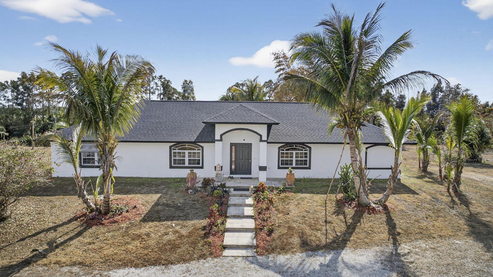 A white single-story house with a dark roof, arched windows, and palm trees in front — 3446 Cabbage Palm Way, Loxahatchee FL 33470, LOXAHATCHEE, FL