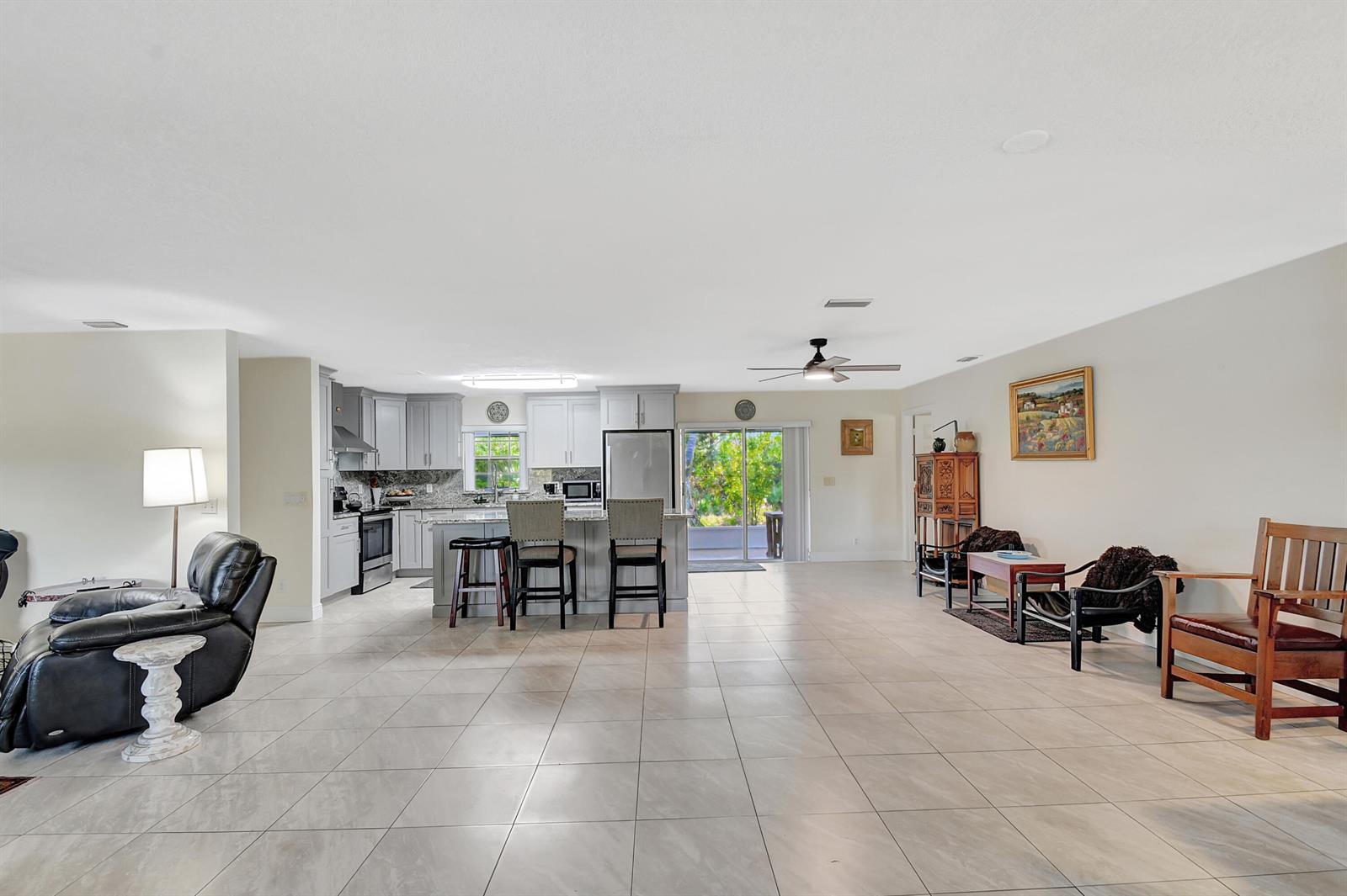 An open-concept living area features a kitchen with grey cabinets, tile flooring, and sliding doors — 3446 Cabbage Palm Way, Loxahatchee FL 33470, LOXAHATCHEE, FL