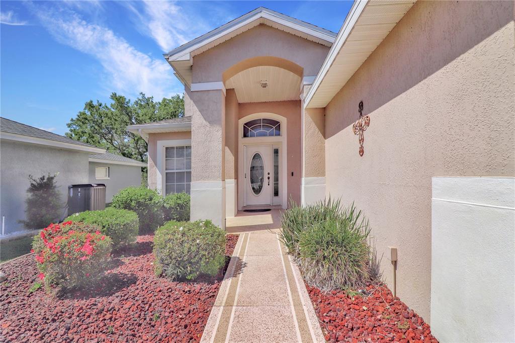 A beige stucco house exterior features a front walkway leading to a white arched doorway — 20751 QUEEN ALEXANDRA DRIVE, LEESBURG, FL