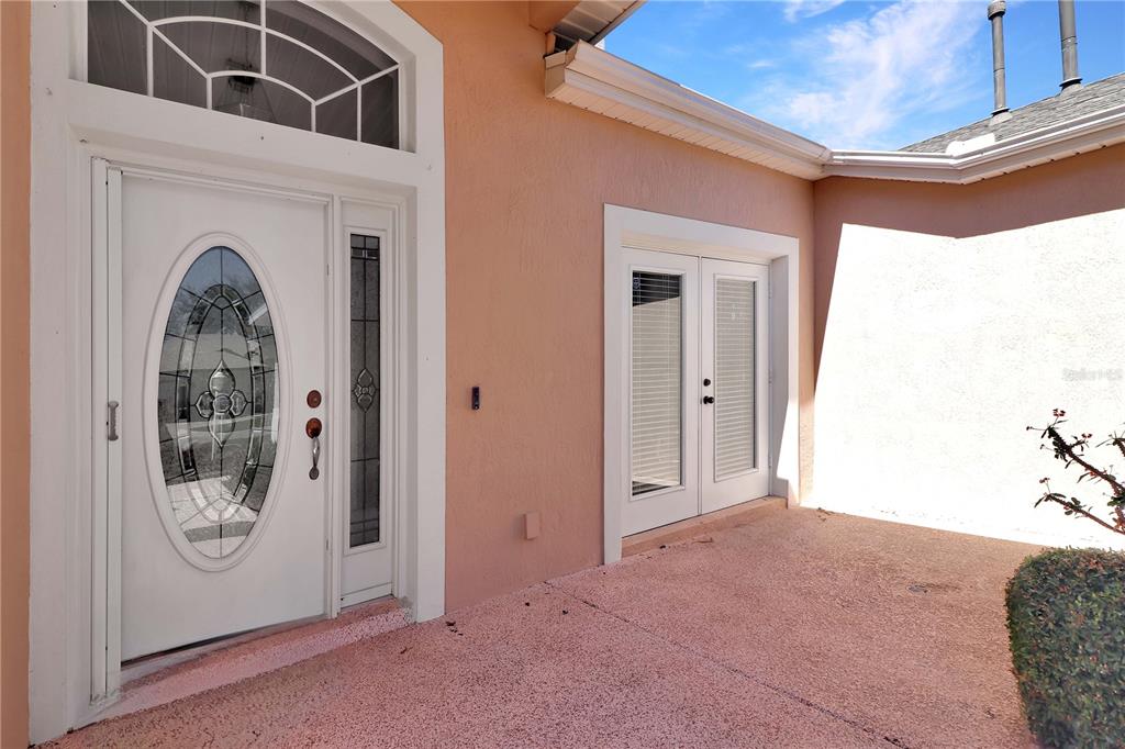 A peach-colored exterior wall features a white front door with a glass oval insert — 20751 QUEEN ALEXANDRA DRIVE, LEESBURG, FL