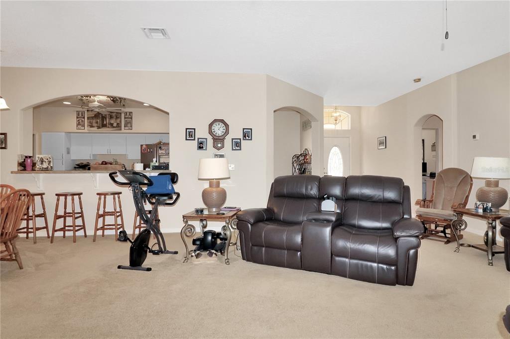 A living room features a dark leather sofa, a stationary bike, and an open kitchen — 20751 QUEEN ALEXANDRA DRIVE, LEESBURG, FL