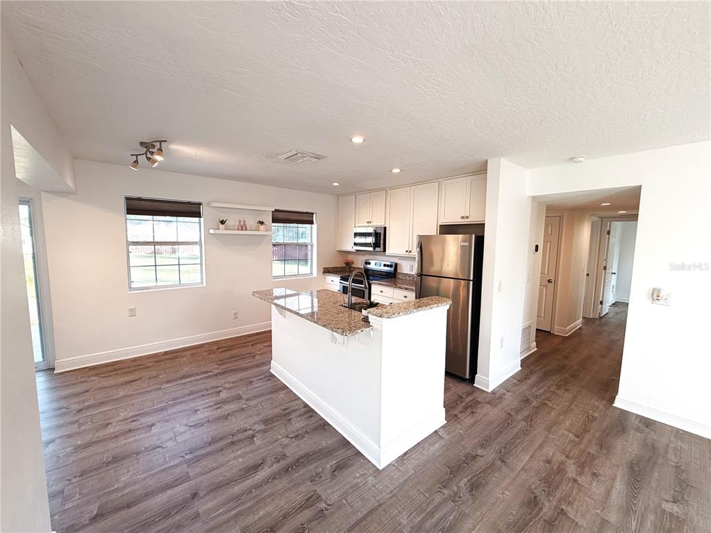 A kitchen with white cabinets, granite countertops, stainless steel appliances, and wood-look flooring — 904 KENSINGTON DRIVE, COCOA, FL