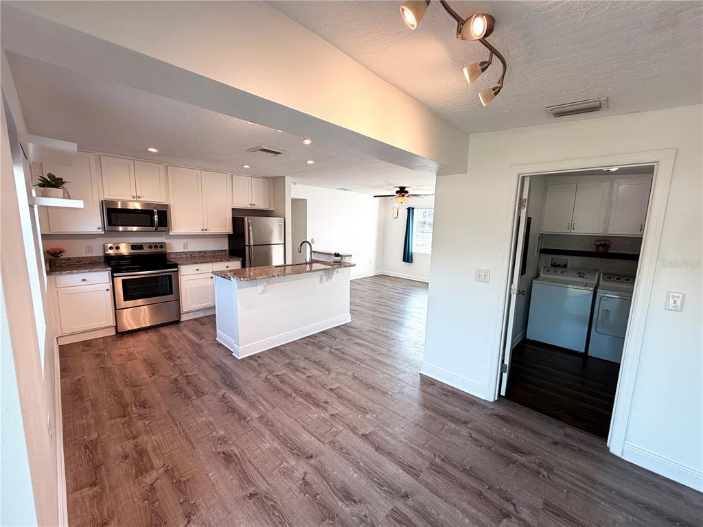 A kitchen with white cabinets, stainless steel appliances, and an island opens to a living area — 904 KENSINGTON DRIVE, COCOA, FL