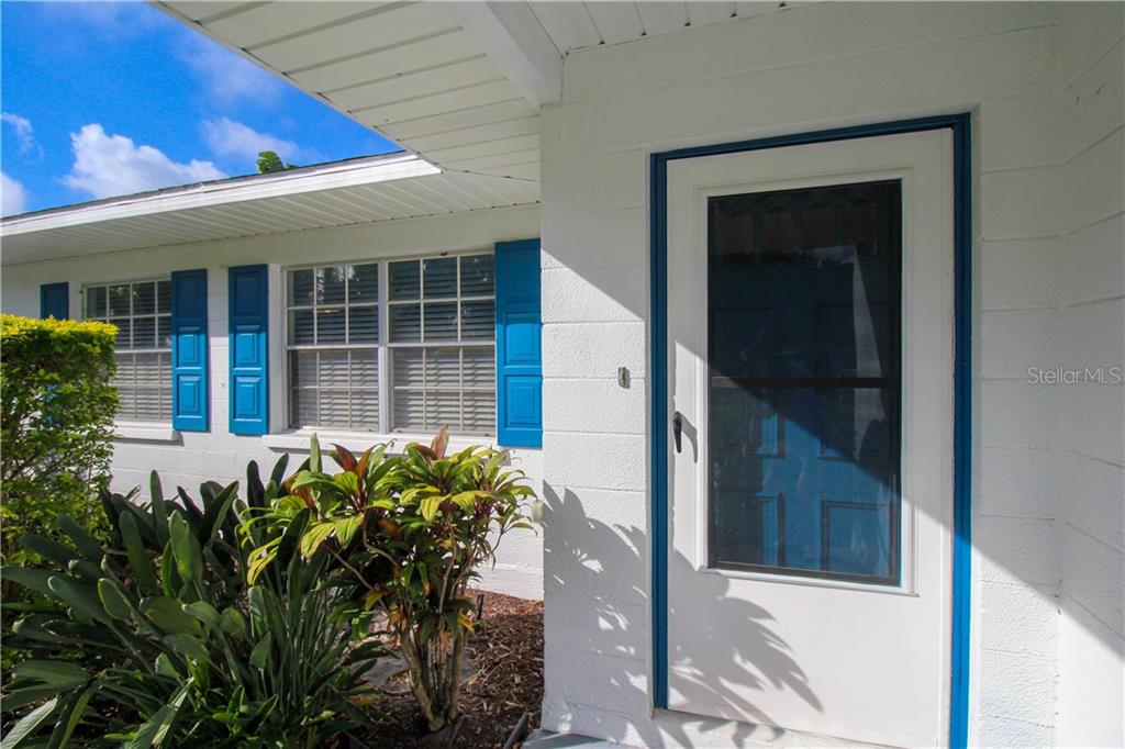 A white house exterior features blue shutters, a front door, and a small garden bed — 2806 TAUNTON DRIVE W, BRADENTON, FL