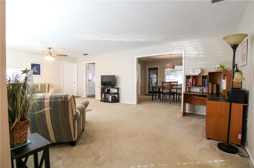 A living room with beige carpet, a striped armchair, a television stand, and a dining area — 2806 TAUNTON DRIVE W, BRADENTON, FL