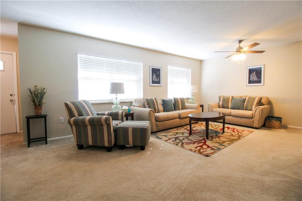A living room features beige carpet, two sofas, a striped armchair with ottoman, and windows — 2806 TAUNTON DRIVE W, BRADENTON, FL