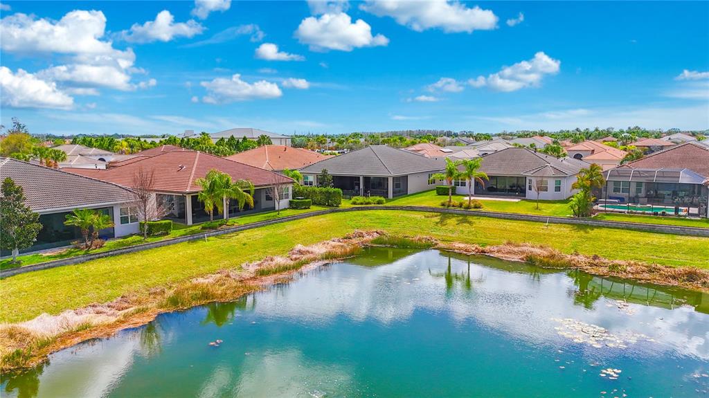 An aerial view shows several suburban houses with tiled roofs overlooking a small pond — 4924 PAMPLONA COURT, WIMAUMA, FL