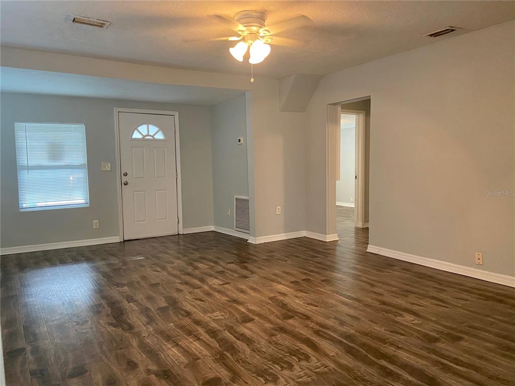 An empty living room features wood-look flooring, light gray walls, a ceiling fan, and a front door — 8105 N 12TH STREET, TAMPA, FL