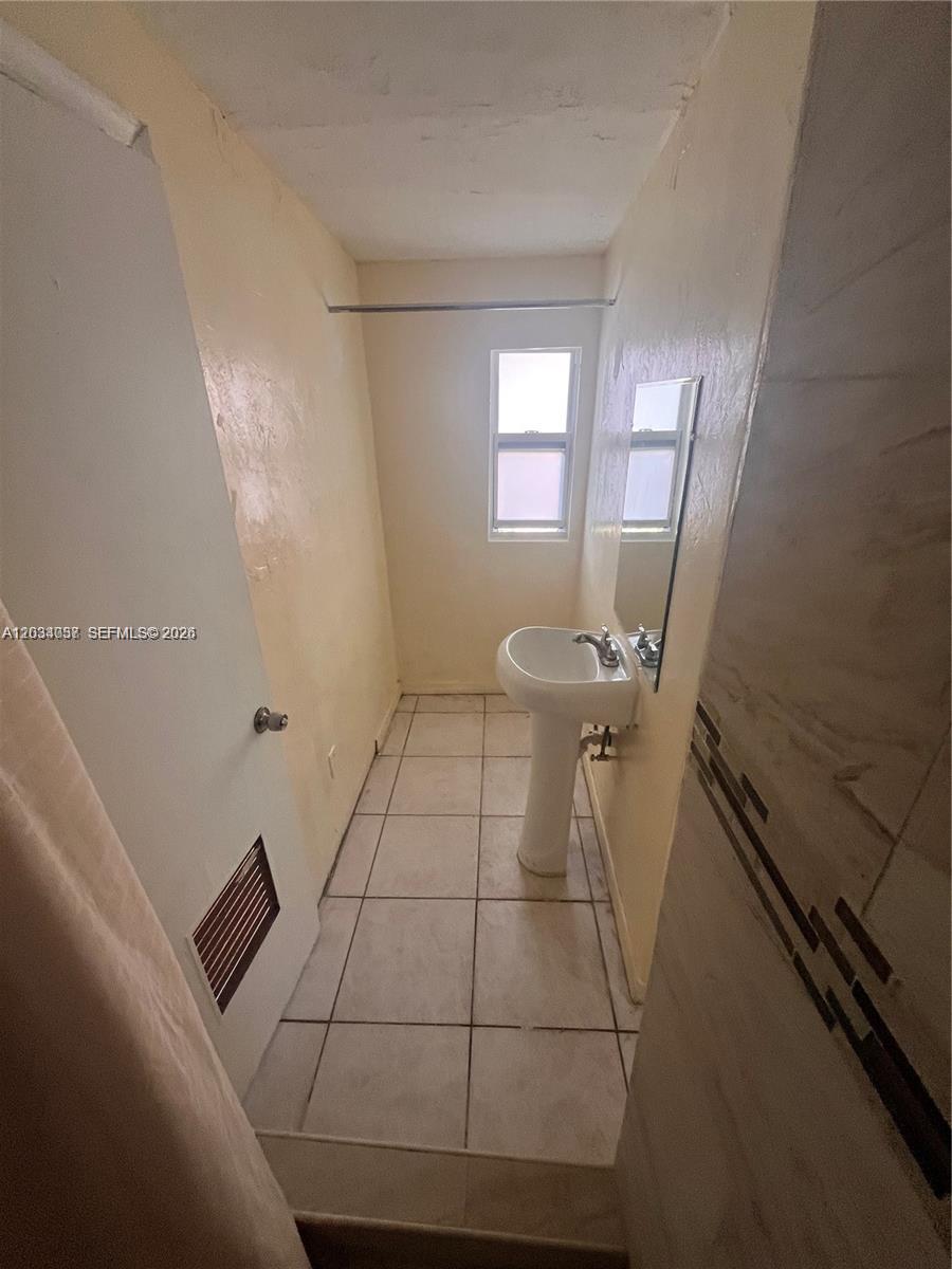 A small bathroom features a pedestal sink, tiled floor, and a window — 13215 NW 19th Ave # 1, Miami FL 33167, MIAMI, FL