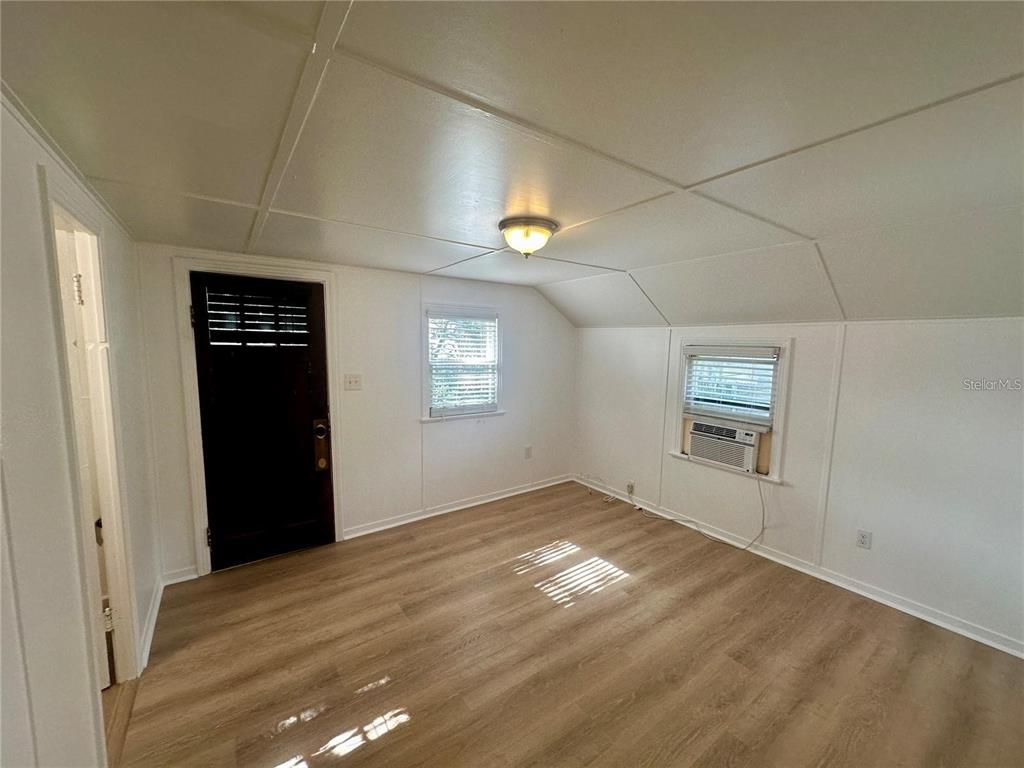 An empty room features light wood-look flooring, white paneled walls, a ceiling light, and windows — 15 1/2 4TH STREET N, LAKE WALES, FL