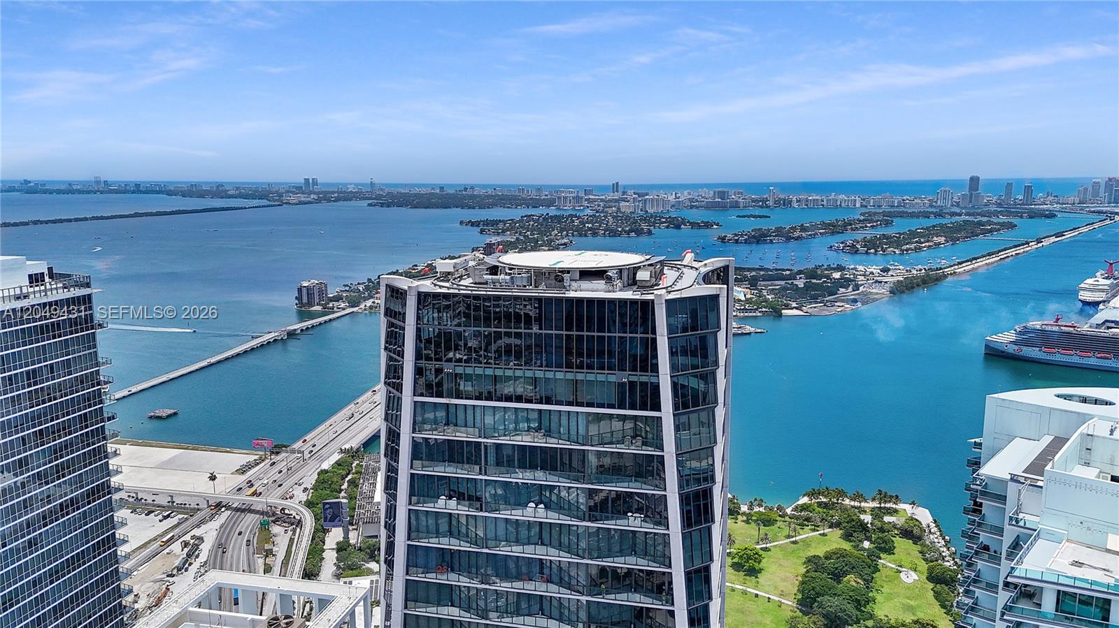 An aerial view shows a modern glass skyscraper with a rooftop helipad near the water — 1000 Biscayne Blvd # 4401, Miami FL 33132, MIAMI, FL