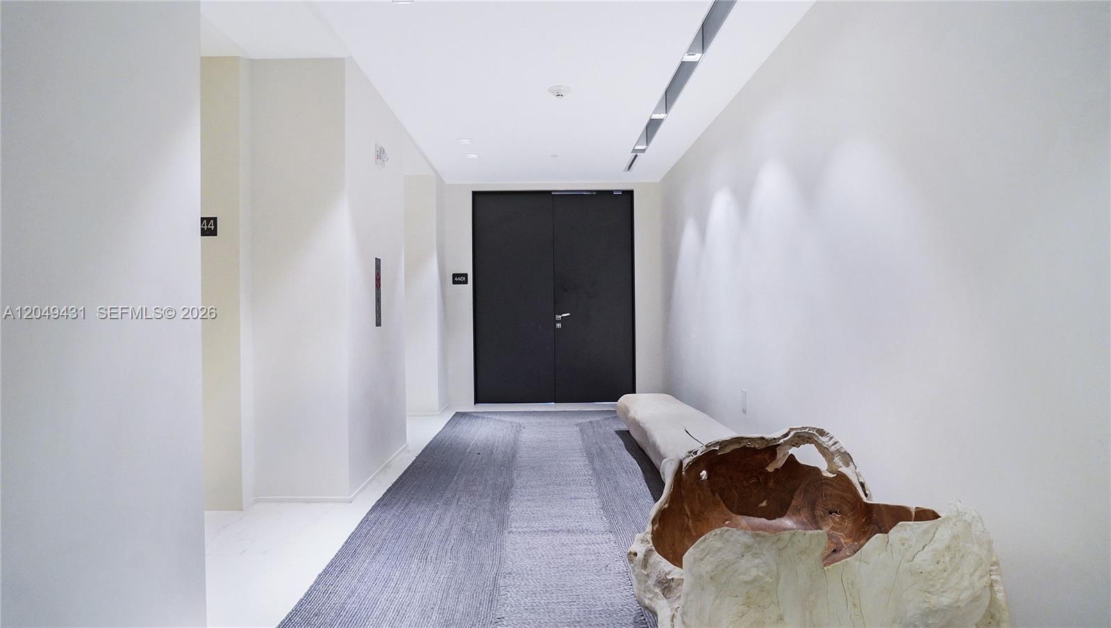 A minimalist hallway features white walls, a dark double door, and a wooden sculpture — 1000 Biscayne Blvd # 4401, Miami FL 33132, MIAMI, FL