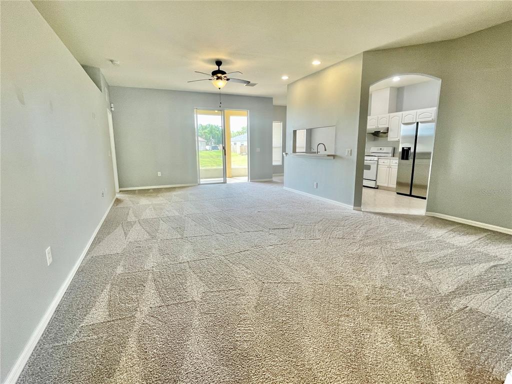 A carpeted living room features a ceiling fan, sliding glass doors, and an arched kitchen entrance — 24652 PORTOFINO DRIVE, LUTZ, FL